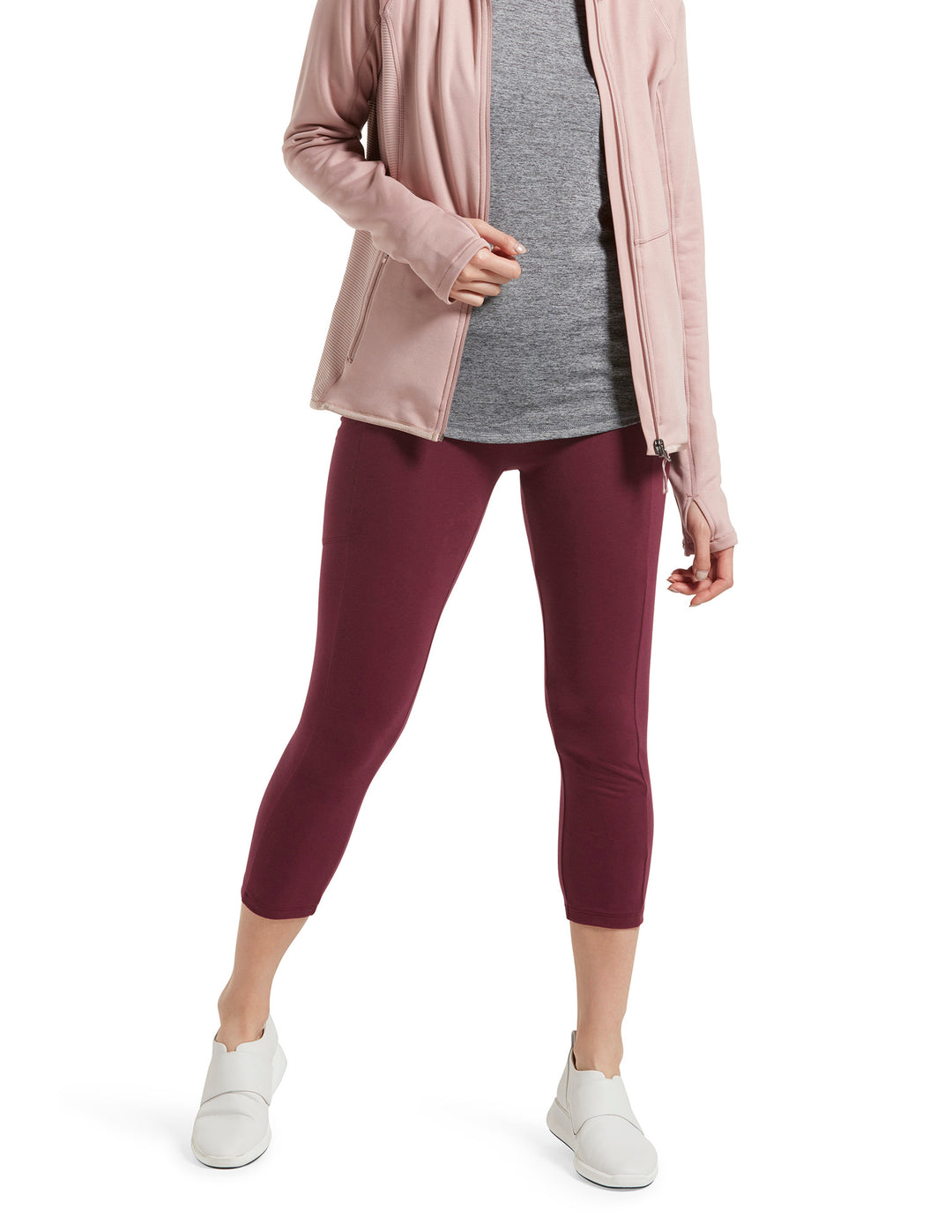 A person wearing red capri leggings with a tech pocket on the side, paired with a grey top and pink cardigan, and white shoes.
