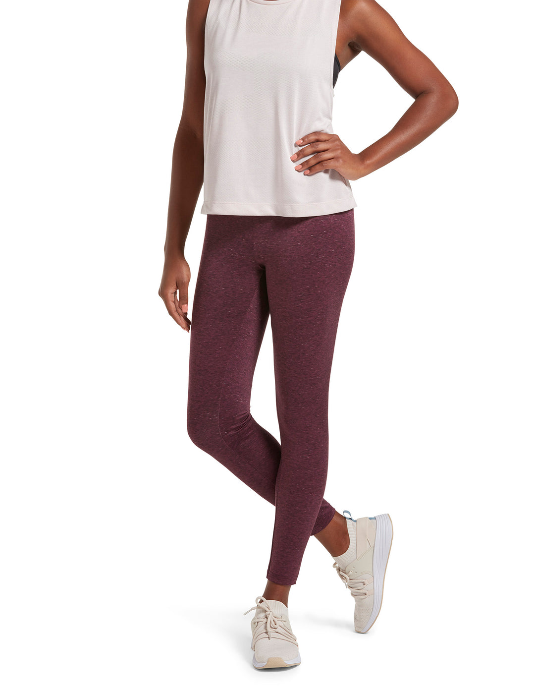 A person wearing full-length black sport leggings with a wide, comfort waistband, paired with a white top and white sneakers.