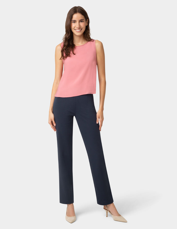 Woman wearing a pink sleeveless top and navy pants on a white background