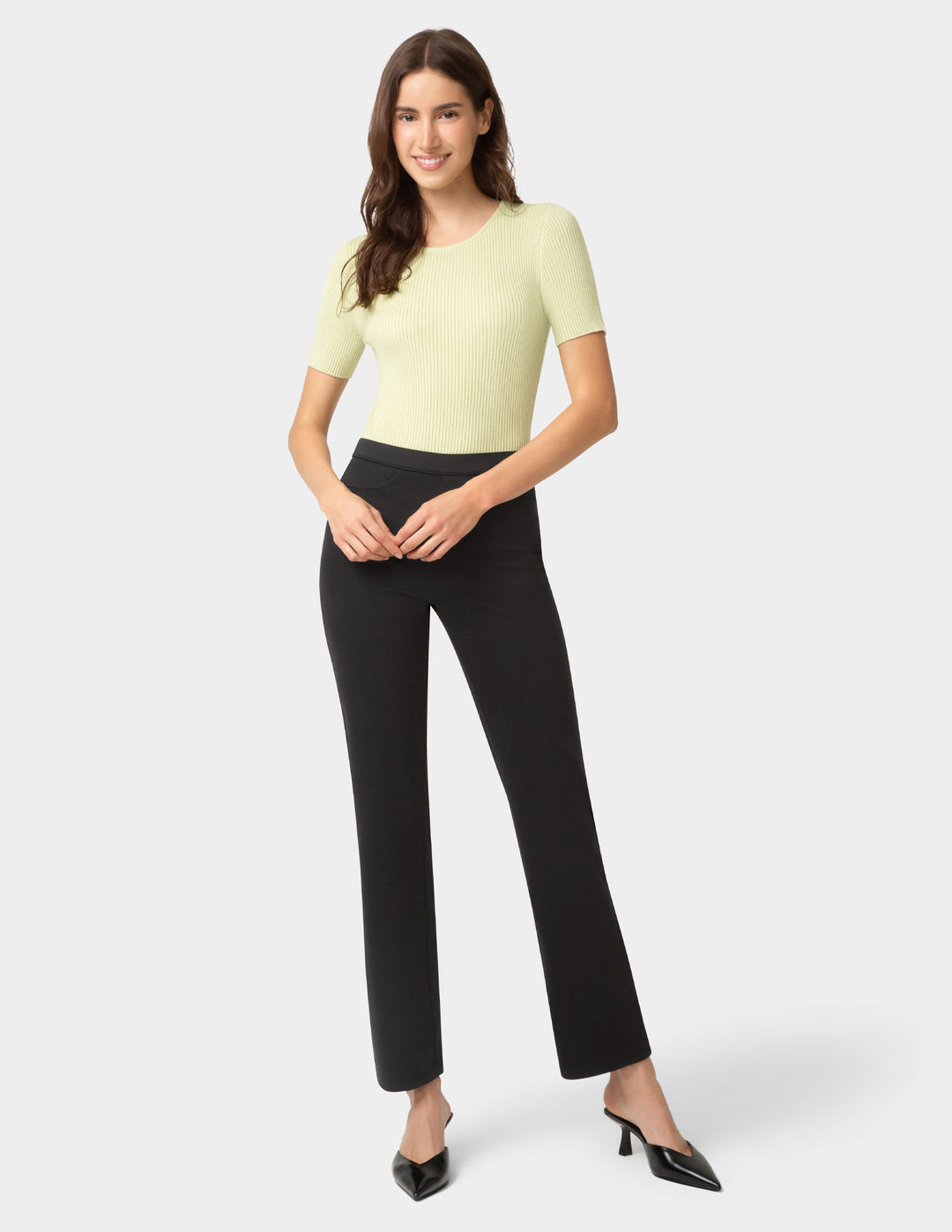 Woman wearing a light green top and black pants on a white background