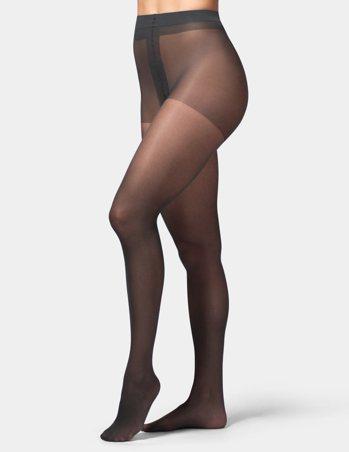 A model's lower body wearing sheer black thigh-high stockings against a light gray studio background.