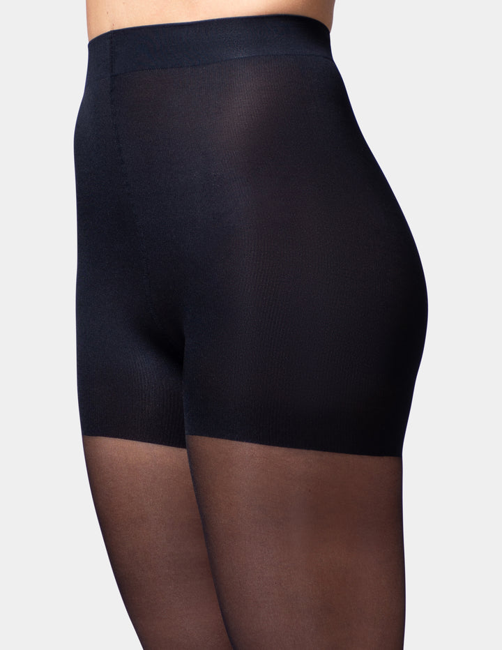 A close-up of a model's wearing sheer black tights, shown from the waist to mid-thigh area against a light gray studio background.