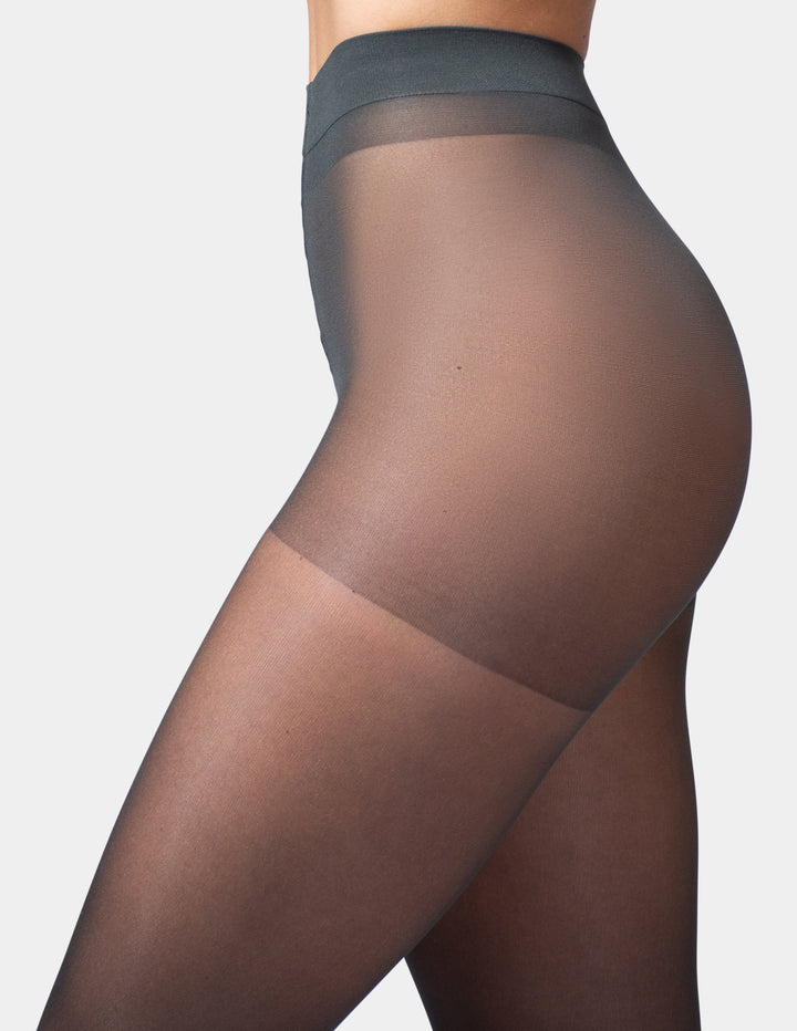 Close-up side view of a model wearing sheer black thigh-high stockings against a light gray studio background.