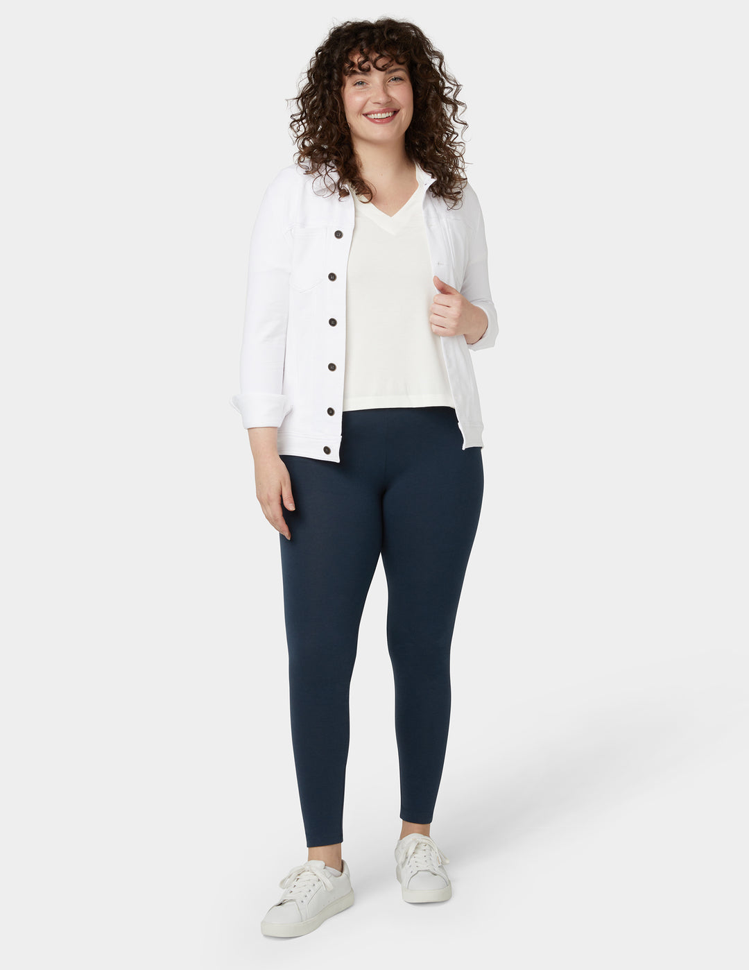 A model wearing navy blue leggings with a white top and a light-colored jacket.