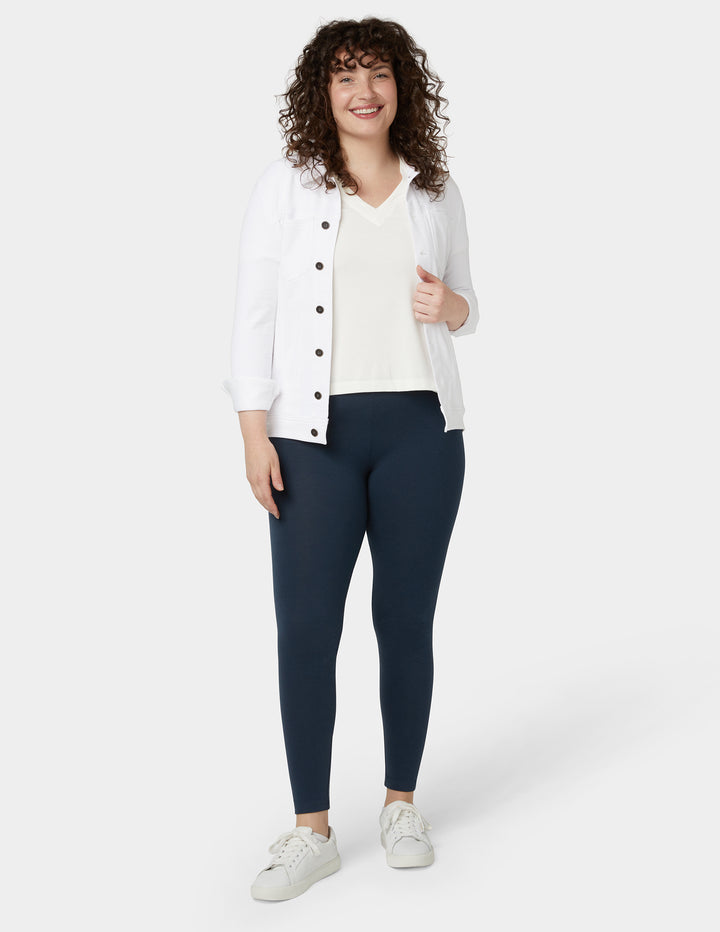 A model wearing navy blue leggings with a white top and a light-colored jacket.
