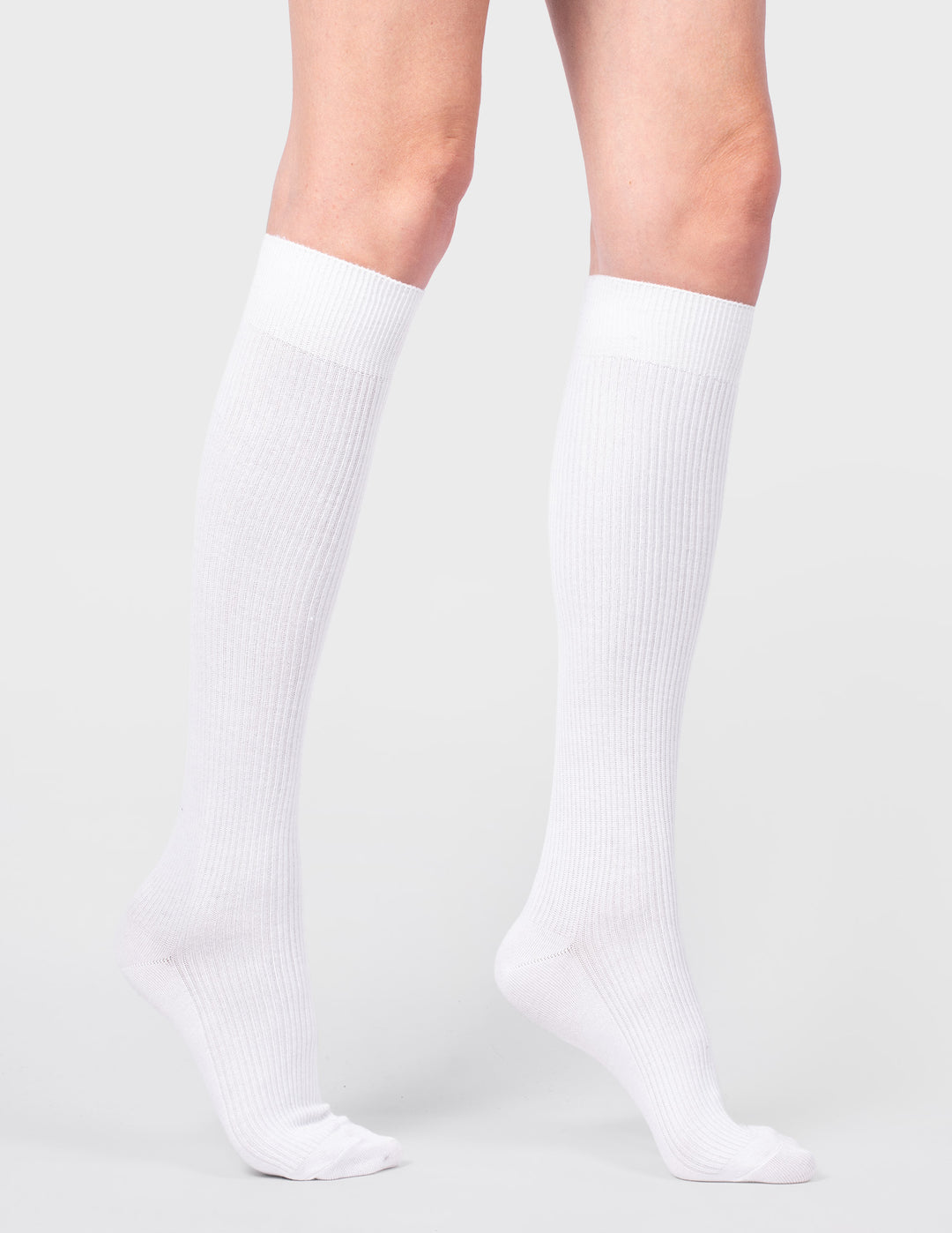 White knee-high socks worn by a person on a light gray background
