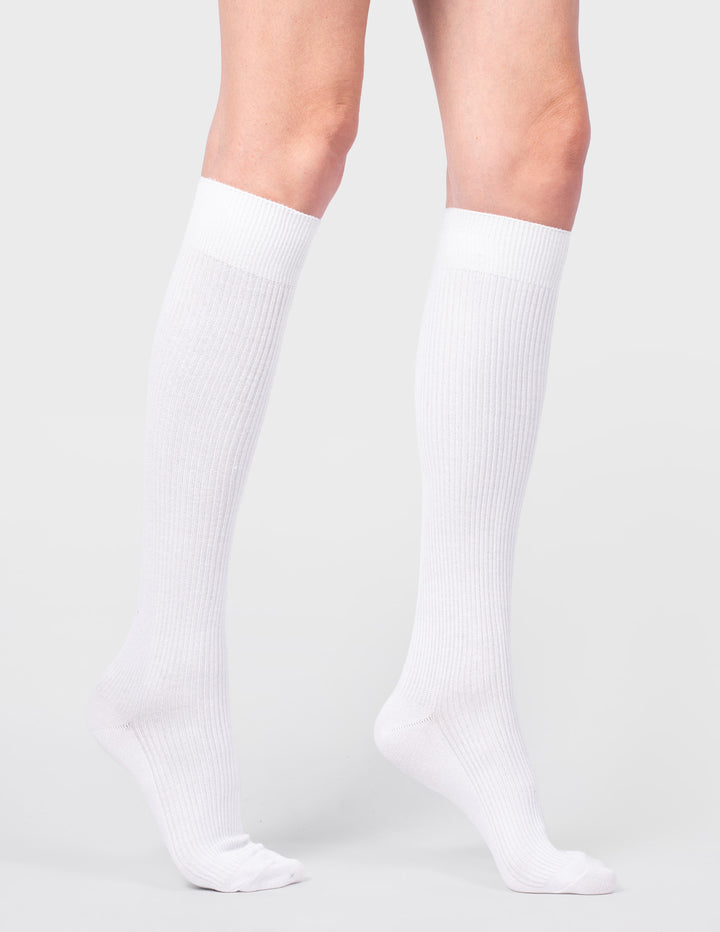 White knee-high socks worn by a person on a light gray background