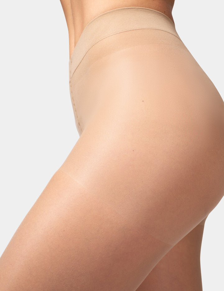 Close-up side view of a model wearing sheer nude thigh-high stockings against a light gray studio background.